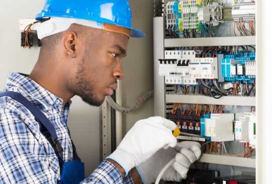 Young African Male Technician Repairing Fusebox With Screwdriver